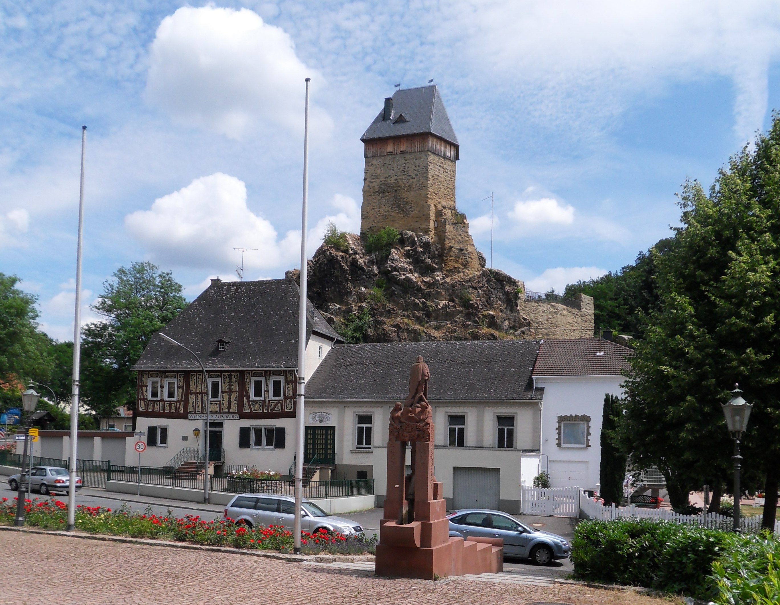 Blick nach Osten vom Kirchvorplatz in Wiesbaden-Frauenstein über den Georgsbrunnen, die Kirschblütenstraße und das „Weinhaus zur Burg“ hin zur Burg und dem Burgfelsen